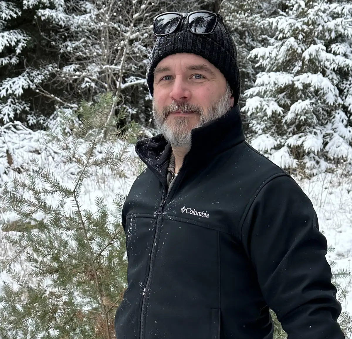 Collin posing for a photo in front of a snowy background of trees.