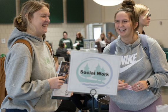 Two students at a career expo holding a sign: Social Work