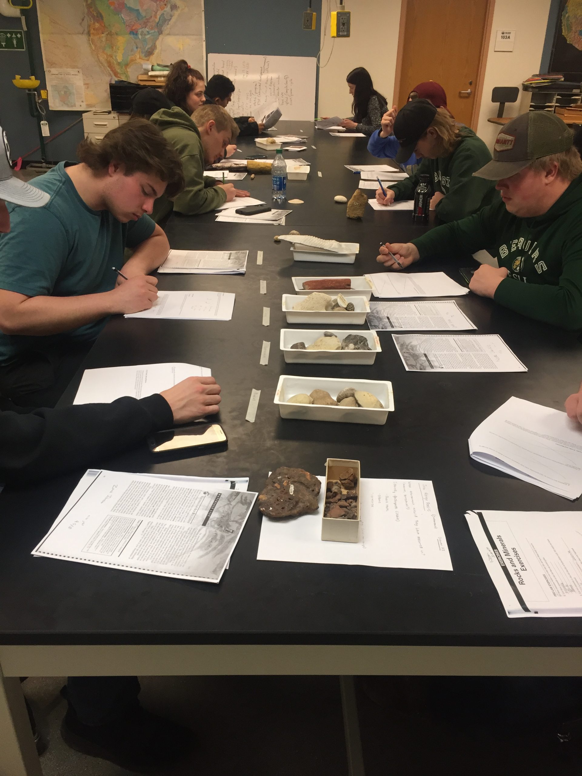 Students sitting on either side of a lab table with trays of rocks and papers in the middle