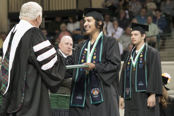 An Indigenous Bemidji State student receiving a diploma on stage