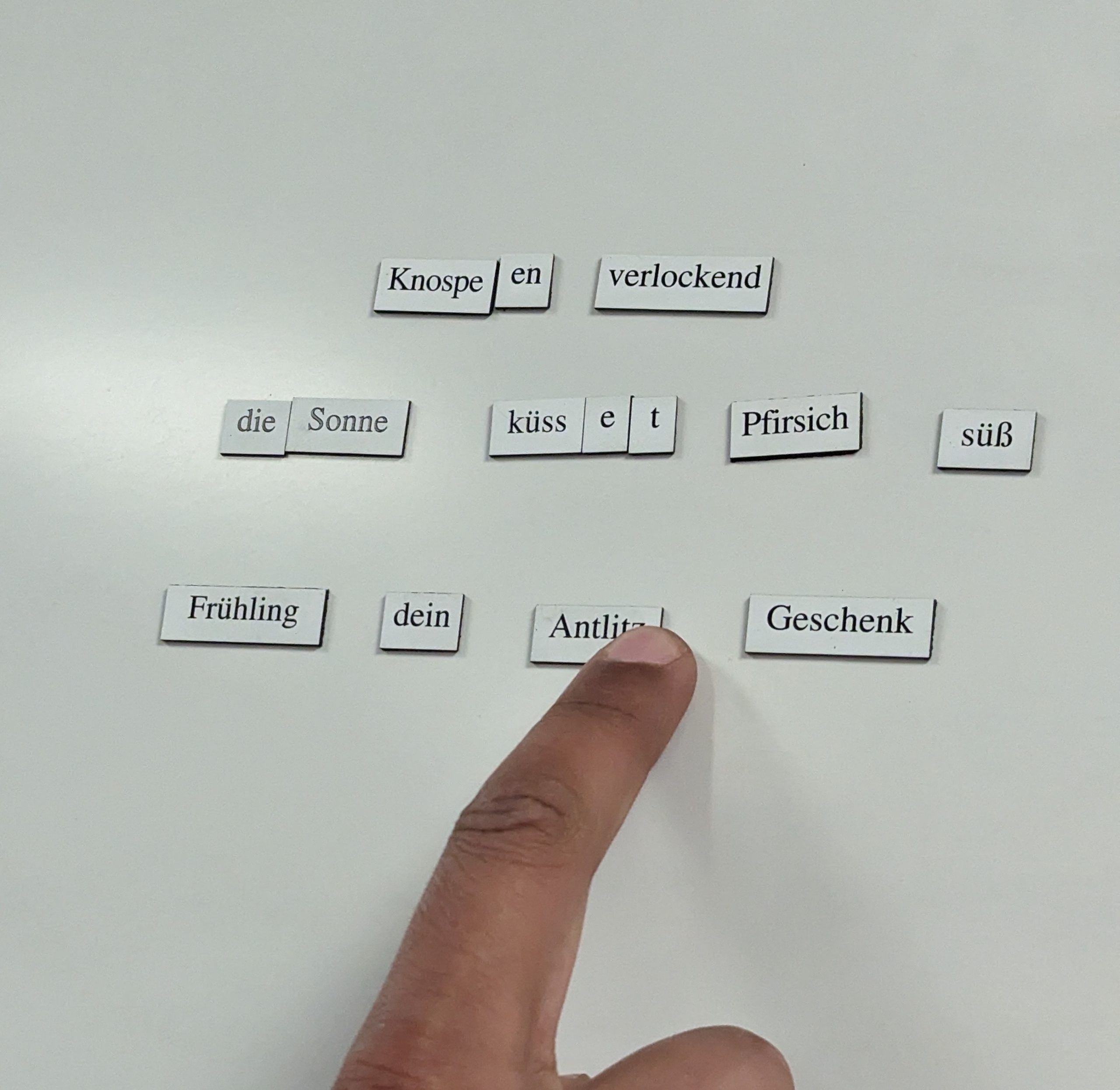 A finger pointing at German words arranged on a white board