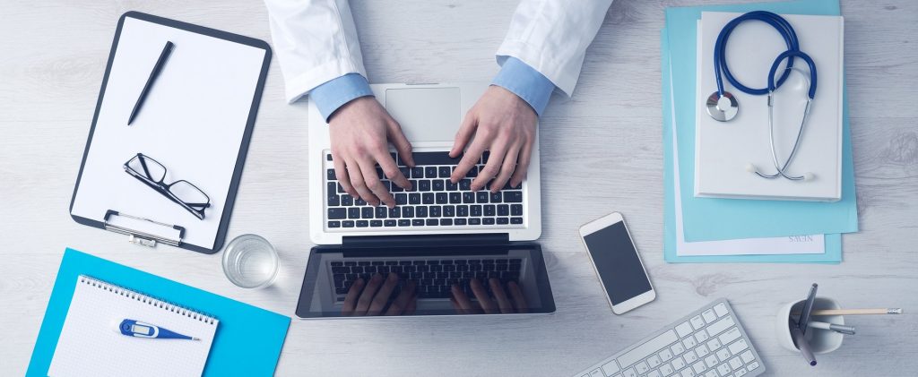 Male hands poised over a laptop keyboard, with the person wearing a lab coat