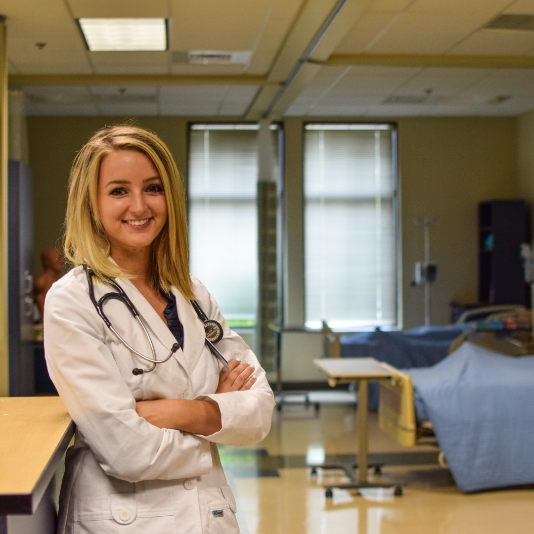 Nursing student in a lab coat in front of an empty hospital bed
