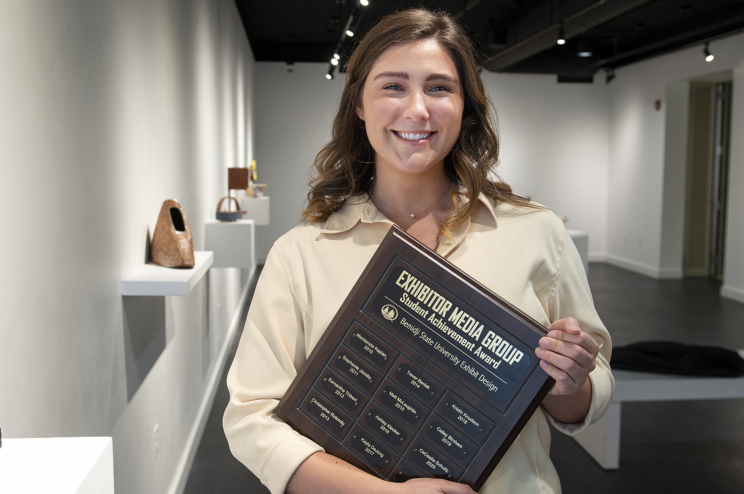 Allison Johanneck holding an exhibitor award in an art gallery at Bemidji State University