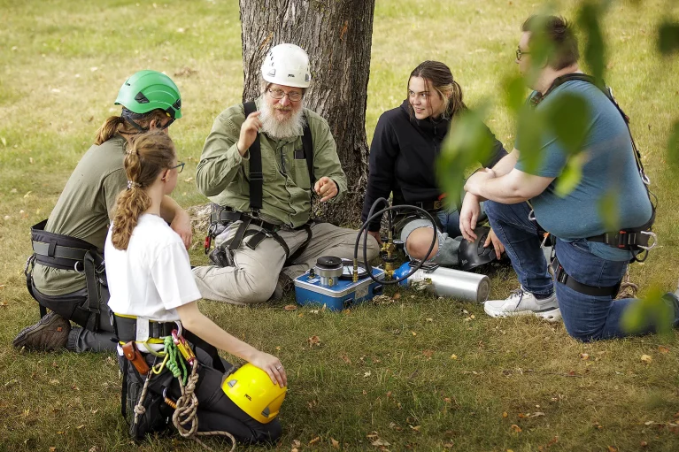 Students and a faculty sitting under a tree discussing how to safely climb.