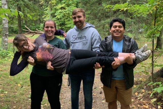 Three Honors students in a forest lifting up another student