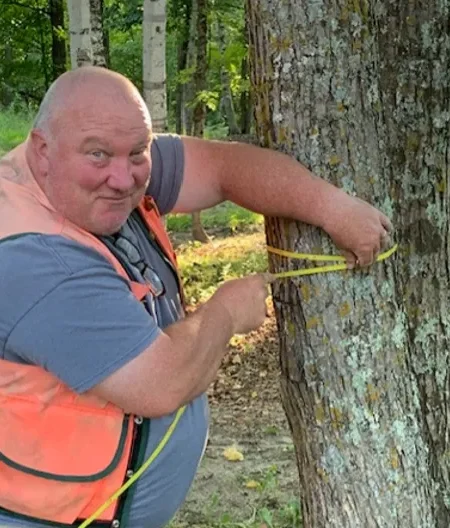 Jim measuring a tree in a safety vest.