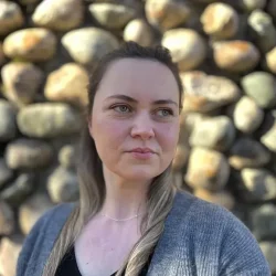 Headshot of Maggie in front of a stone wall.