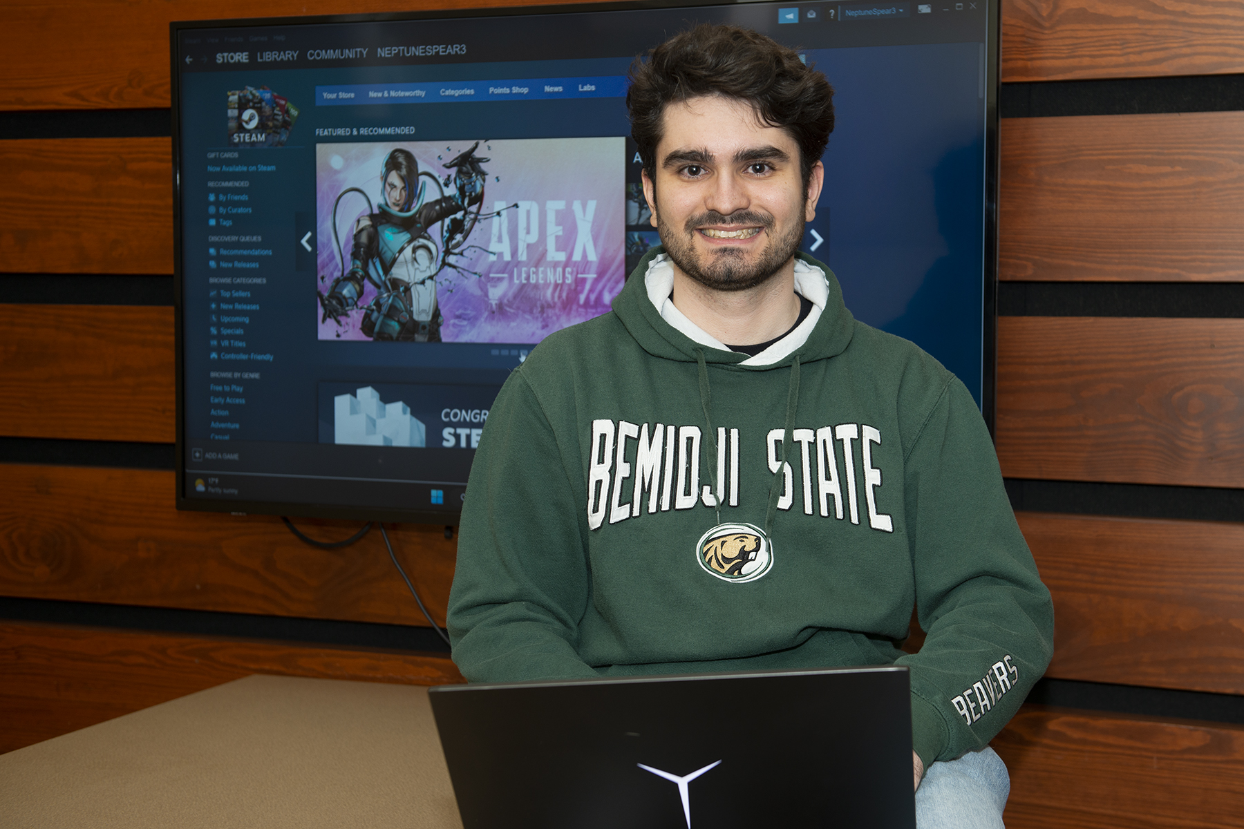 Ben Vossen holding a laptop and sitting in front of a TV screen