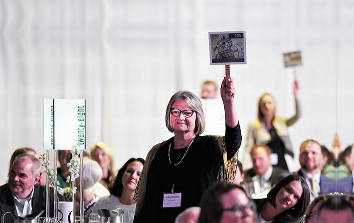 A woman stands up and holds up a bidding sign