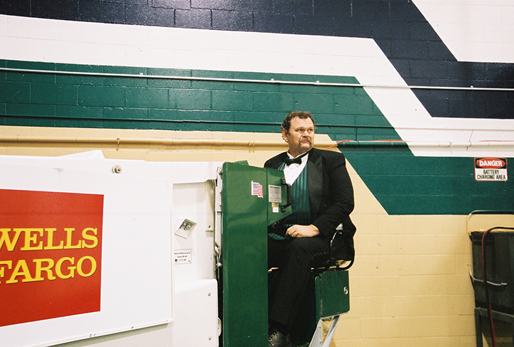 Vance Balstad wearing a green vest and bowtie and black suit jacket driving a Zamboni
