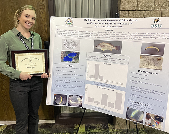 Marissa Pribyl standing in front of a poster and holding a plaque