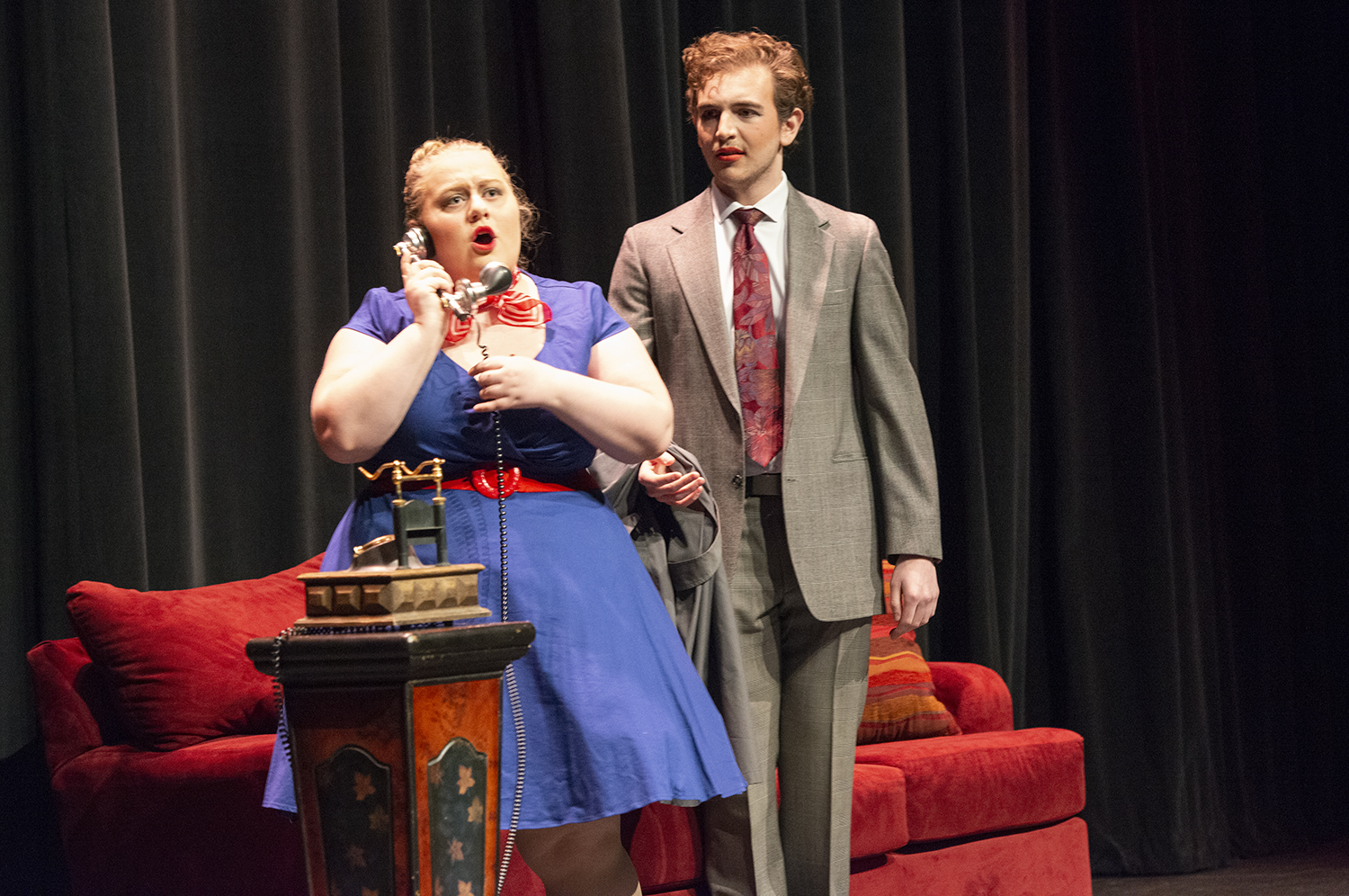 Performance of "The Telephone", a woman talking on the telephone sits on a couch while a man stands impatiently