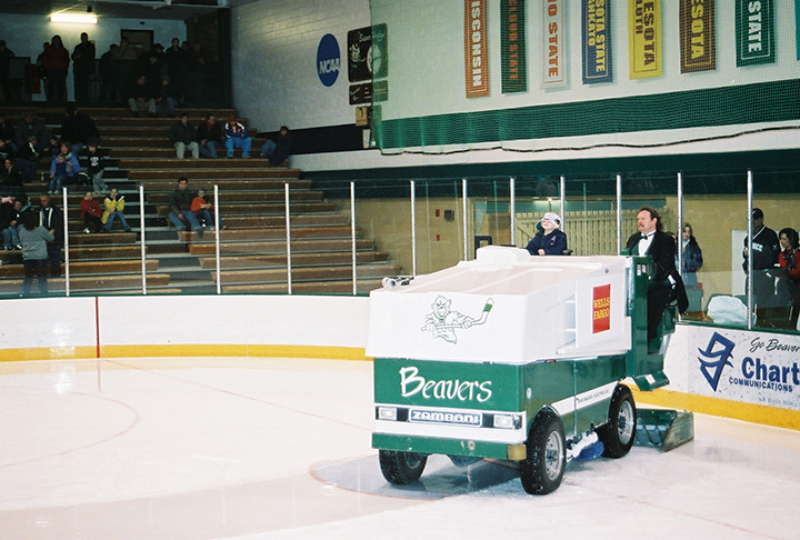 Vance Balstad wearing a green vest and bowtie and black suit jacket driving a Zamboni