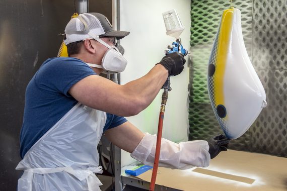 Student sprays a large fishing lure with paint