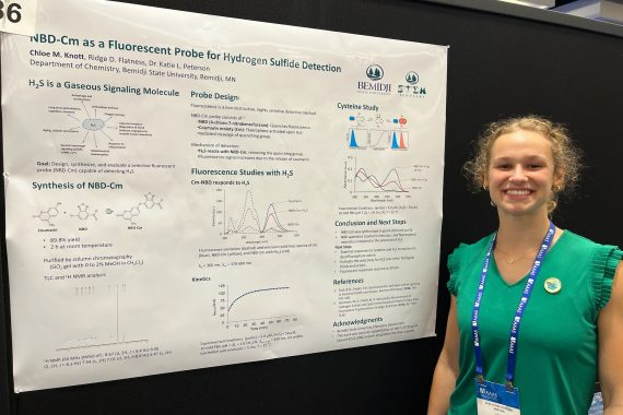 Student Chloe standing next to her research poster while presenting at a conference.