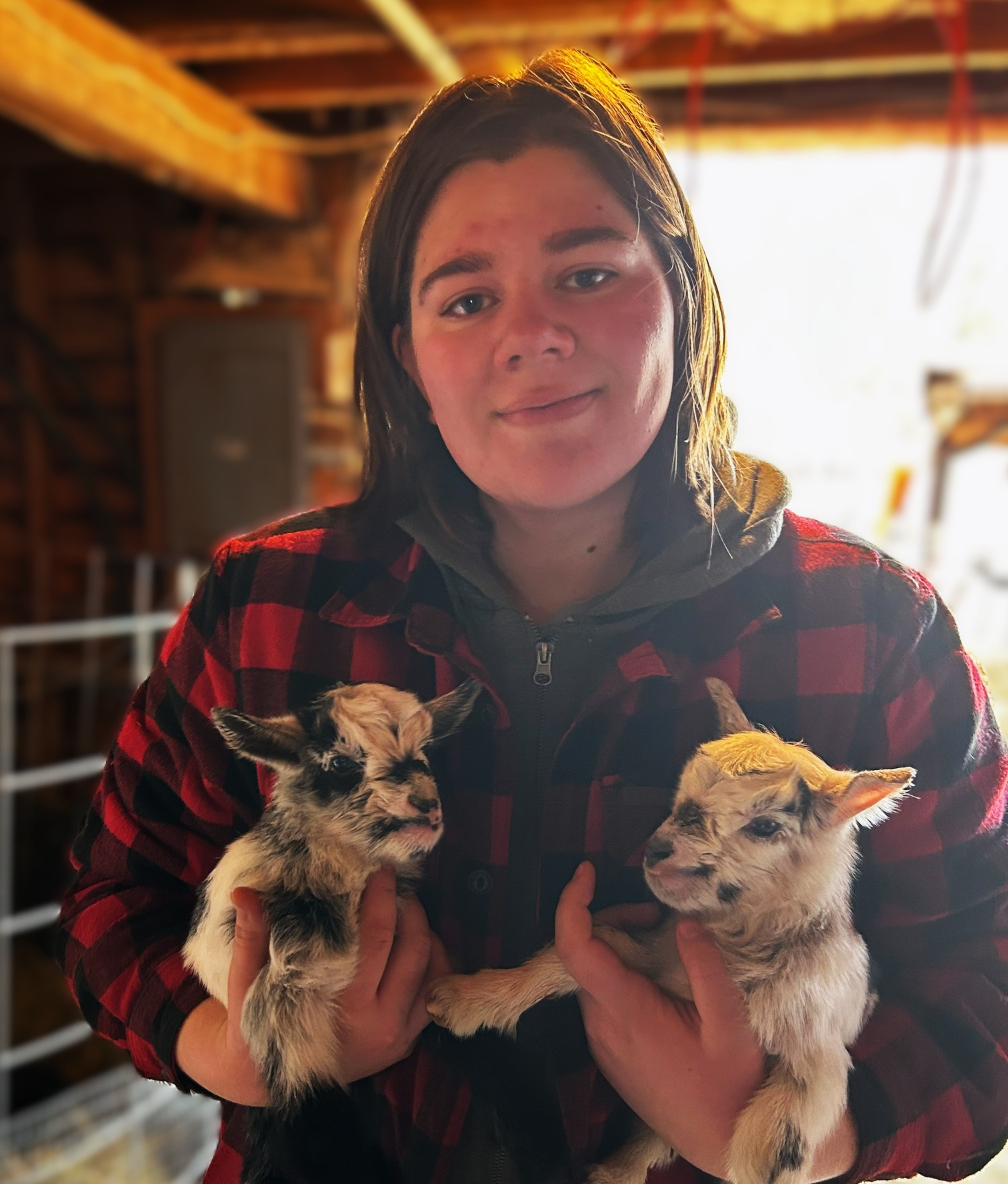 Makaela is standing in a barn and holding two baby goats.