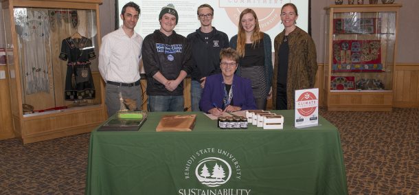 President Faith Hensrud signs Second Nature's Climate Commitment while Jordan Lutz, sustainability project manager, Connor Newby, student senate president, Corrie Stockman, student senate vice president, Anna Hayes, student senator and sustainability office employee and Erika Bailey-Johnson, sustainability coordinator, look on.