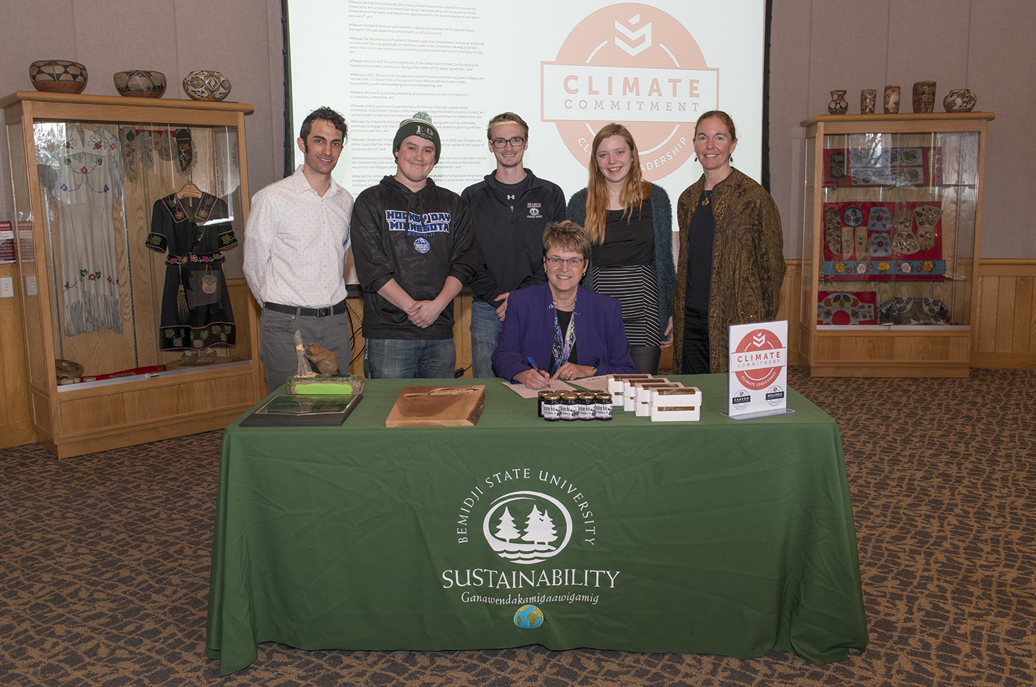 President Faith Hensrud signs Second Nature's Climate Commitment while Jordan Lutz, sustainability project manager, Connor Newby, student senate president, Corrie Stockman, student senate vice president, Anna Hayes, student senator and sustainability office employee and Erika Bailey-Johnson, sustainability coordinator, look on.