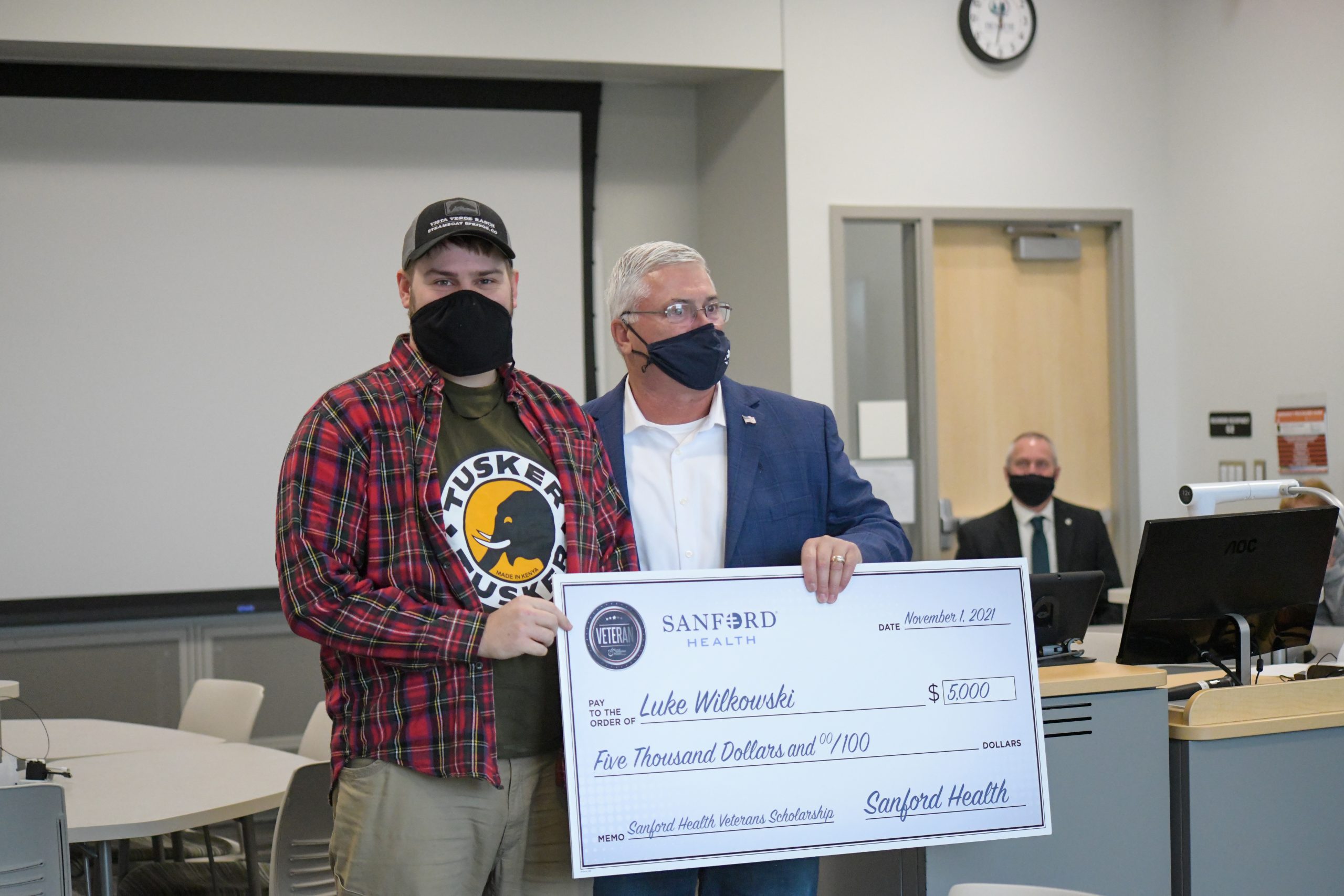 Captain Paul Weckman, director of veteran and military affairs at Sanford Health, presents an oversized check of $5000 to junior nursing student Luke Wilkowski, a veteran Specialist in the U.S. Army.