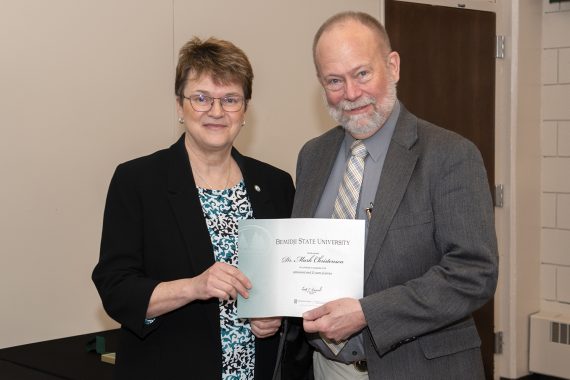 President Faith Hensrud presenting Dr. Mark Christiansen, professor of English, a retirement certificate.