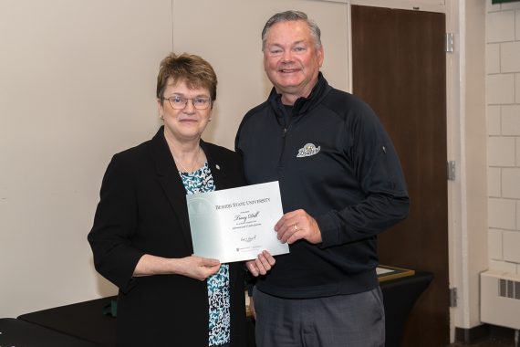 President Faith Hensrud presenting Tracy Dill, director of athletics, a retirement certificate.