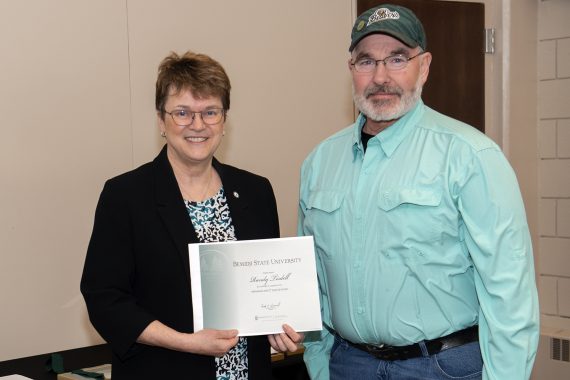 President Faith Hensrud presenting Randy Tisdell, general maintenance worker, a retirement certificate.