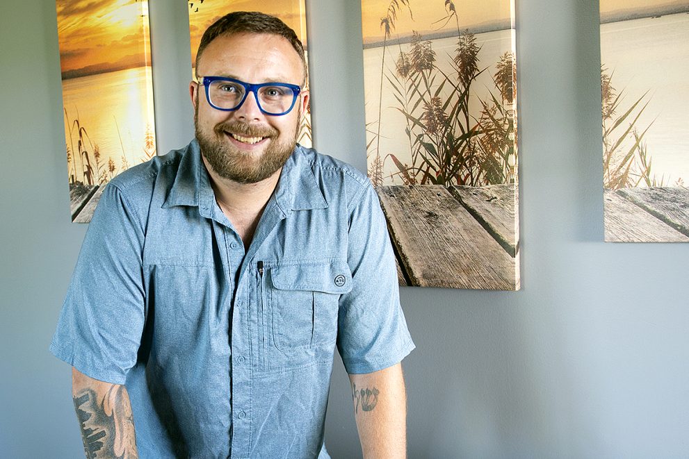 Zach Gordon standing in his Mission Restart office in Grand Rapids and holding a book called “Getting them sober”