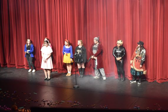 Students standing in costumes on a misty stage