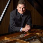 Stephen Carlson poses next to a piano