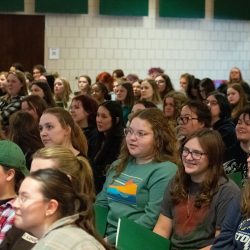 A group of sitting students listens to a presenter