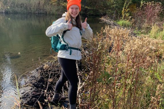 A BSU student poses for a photo on top of a beaver dam