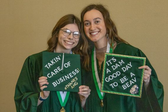 Two graduates pose for a photo with their graduation caps