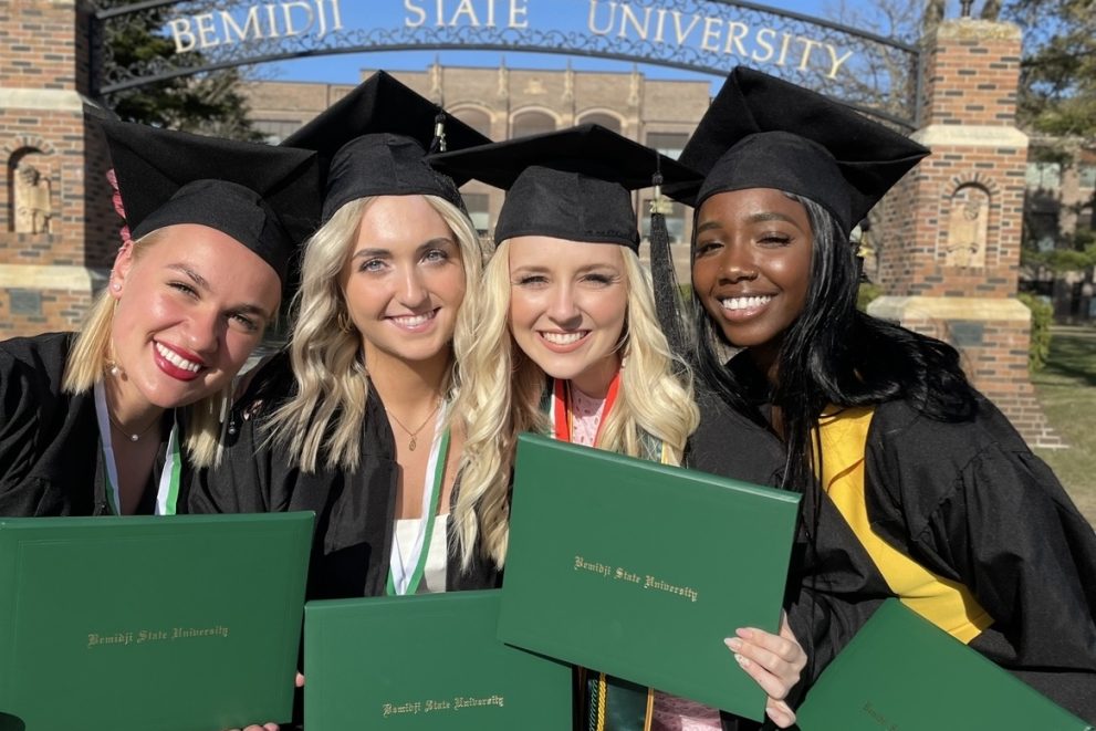 BSU students pictured in front of the BSU arch with their graduation caps and gowns