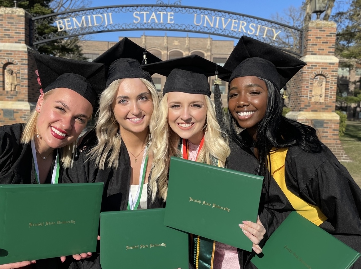 BSU students pictured in front of the BSU arch with their graduation caps and gowns