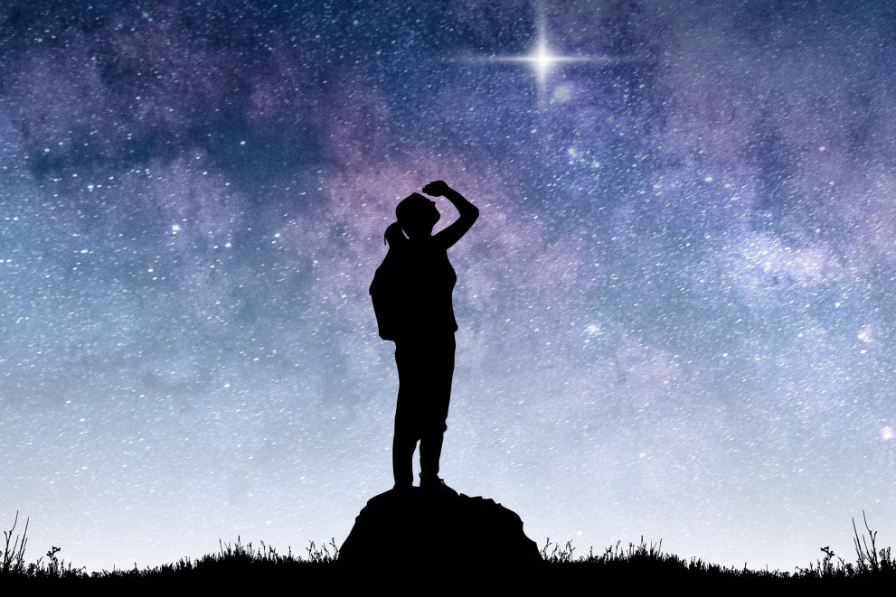 Black silhouette of woman gazing up at a bright star in the sky