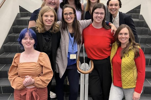 Eight students in Dr. Jennifer Olson's vocal studio pose with her on a set of stairs.