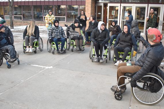A group of people using wheelchairs listen to a BSU faculty member