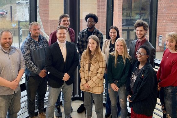 Students and their faculty advisor pose in front of the window in the Memorial Hall stairway, overlooking the BSU campus.