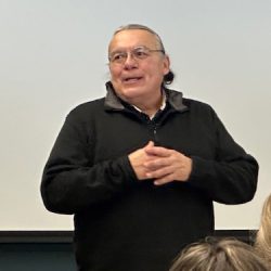 A man with glasses, grey hair and a black sweater.