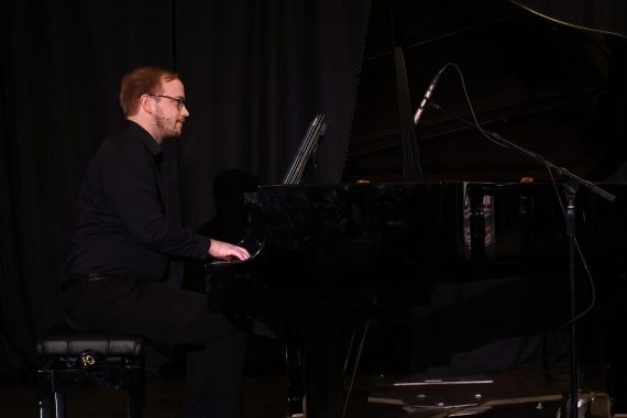 A side view of a man with glasses playing a black Steinway grand piano.