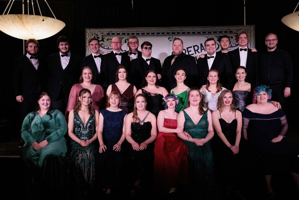 A group of 25 performers wearing formal attire, posed in three rows.