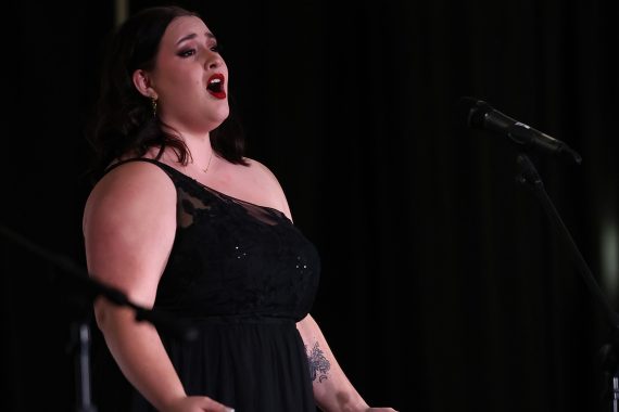 A side view of a woman in a black dress singing.