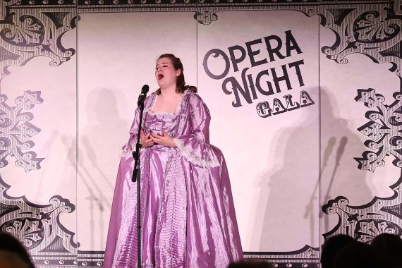 A woman in a pink Victorian dress sings in front of a banner which reads "Opera Night Gala"