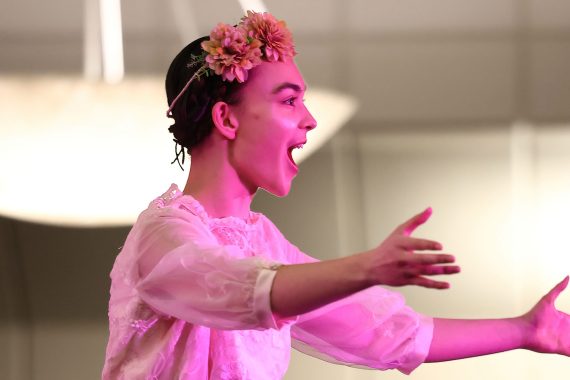 A woman with flowers in her hair singing in pink lighting.