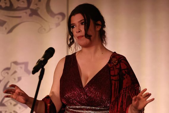 A woman in a red dress is singing, with her hands out at her sides.