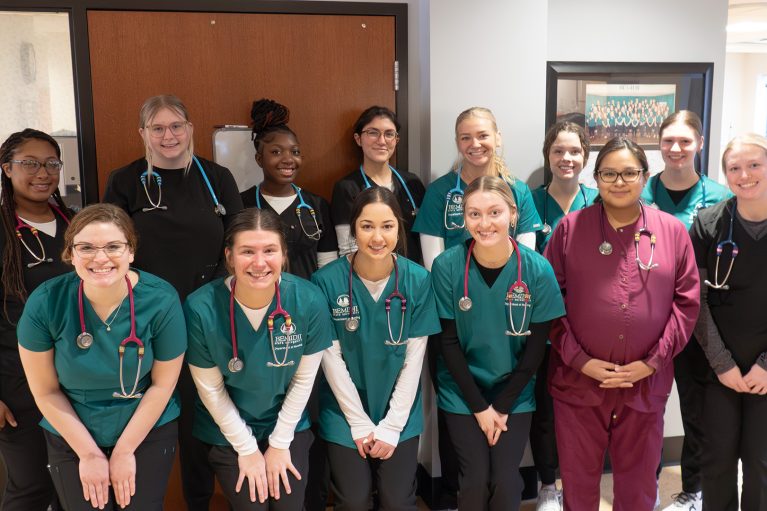 a group of students in nursing scrubs poses in front of a door