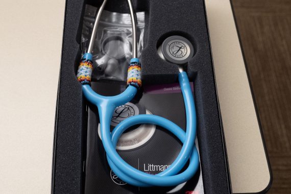 A blue stethoscope in its box, which has hand-beaded bands on each ear tube.