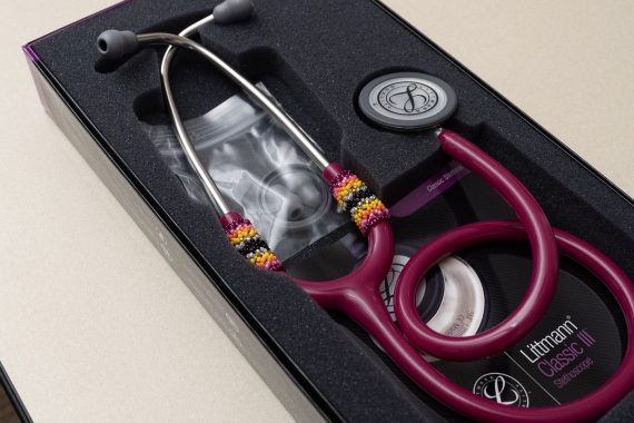 A dark red stethoscope in its box, which has hand-beaded bands on each ear tube.
