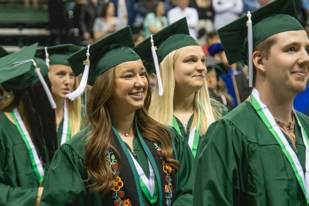 Smiling graduates in green caps and gowns at Bemidji State University commencement.